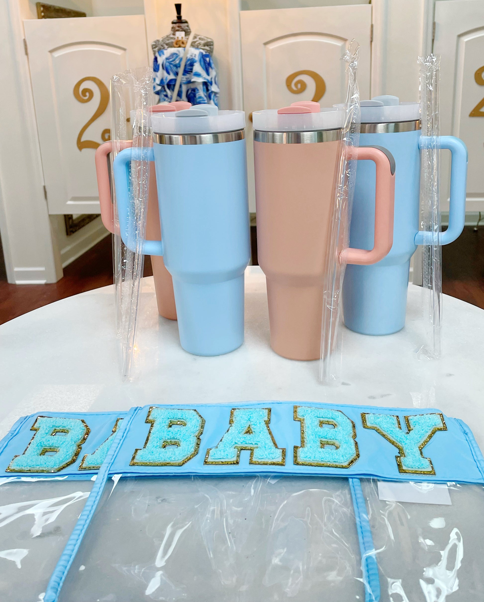 Clear zippered pouch that has a light blue border with the word 'baby' embroidered at the top in chenille light blue varsity letters outlined in shiny gold.