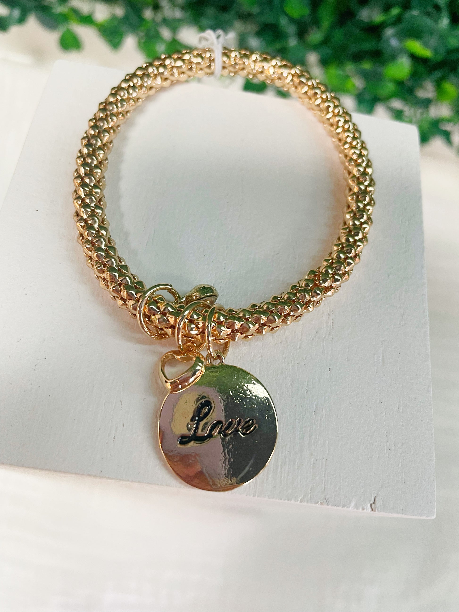 Gold bracelet with a gold charm that says "Love"