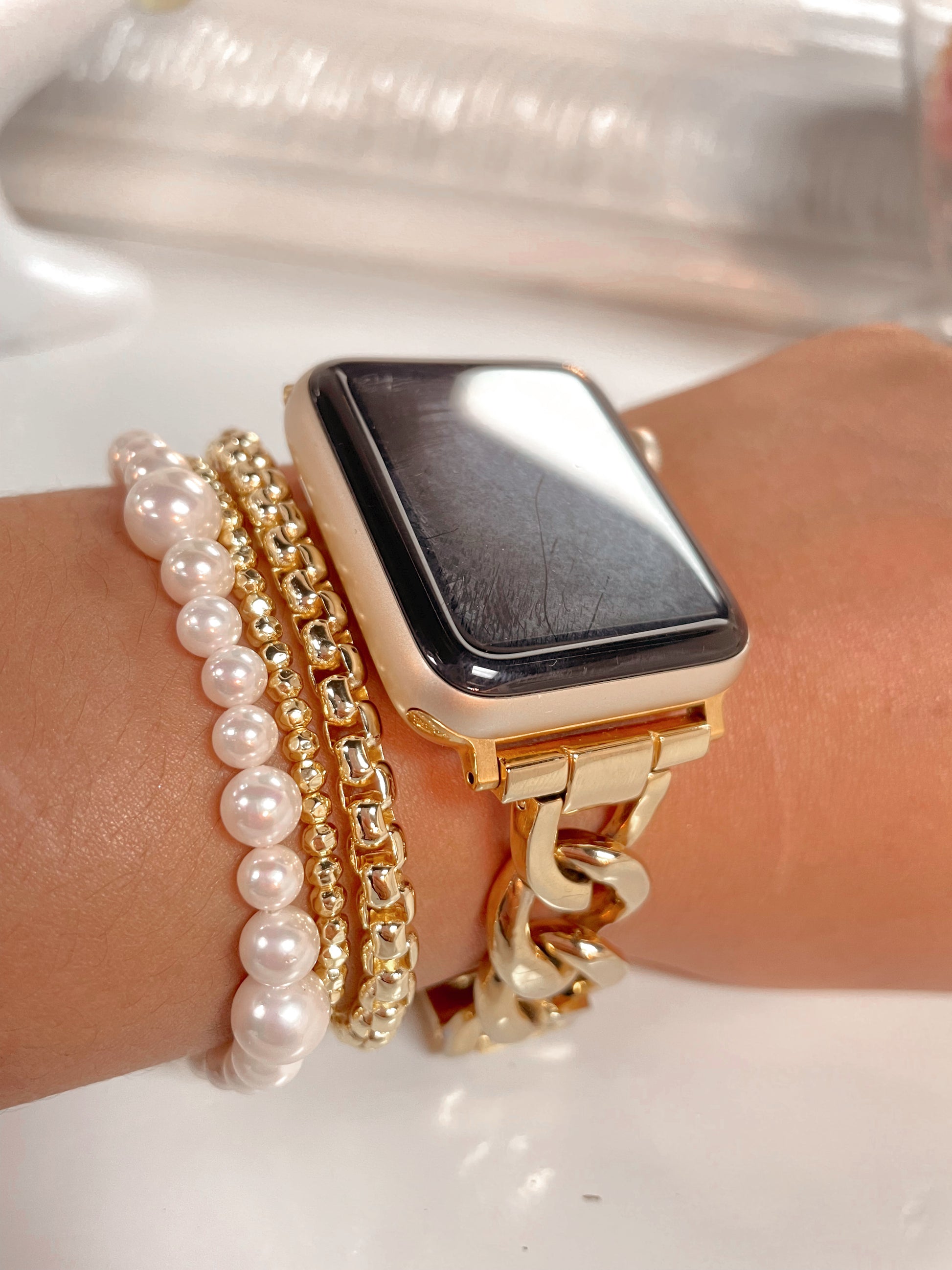 Gold chain link apple watch band stacked with a pearl bracelet and 2 other gold bracelets